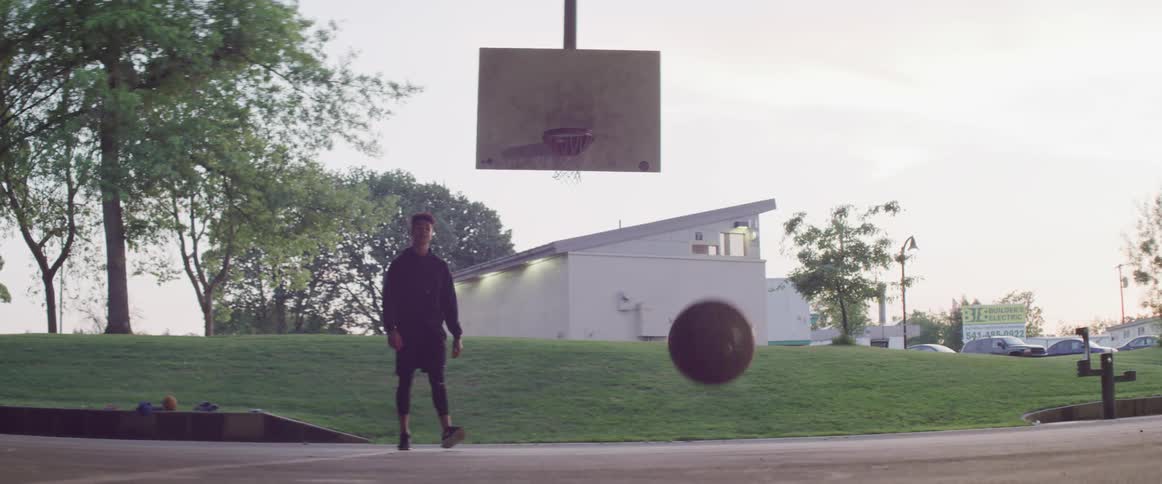 A man walks after a ball that is bouncing away from the hoop