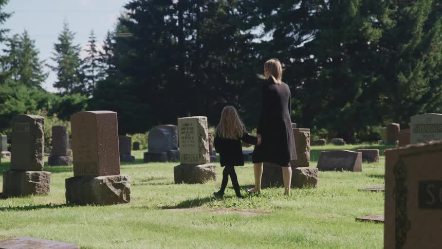 Mother and daughter holding hands walking in a cemetery pass tombstones at daytime