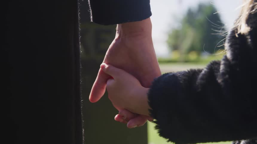 Little girl reaching out to hold her mothers hand at a cemetery