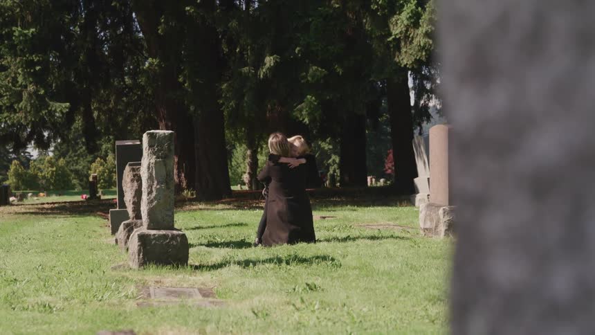 Mother and daughter hug each other in grief near a gravestone on the cemetery at day time