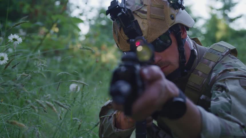 A soldier scans an area in a forest with a snipe gun scope during the day