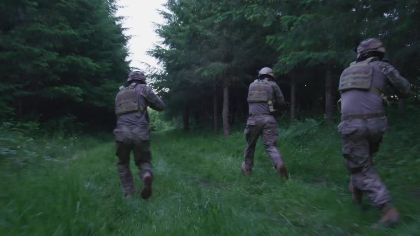 Group of military soldiers running on a trail throught the forest pointing weapons around