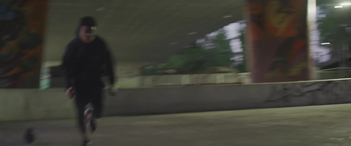 A young man does a dash under a bridge covered in graffiti in the evening