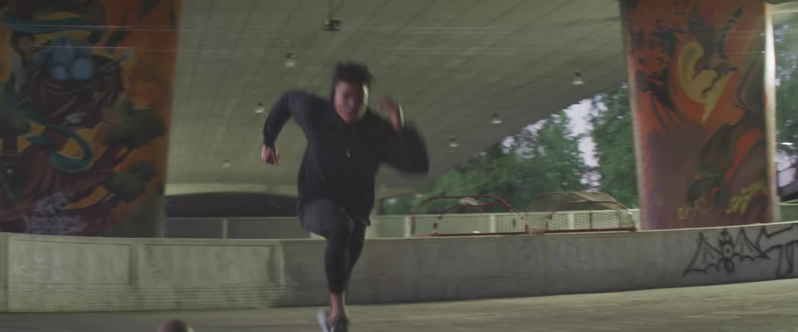A person in all black sprints under a bridge outdoors