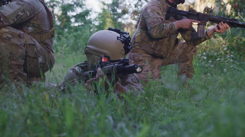 Soldiers crouched down in a forest with their guns drawn