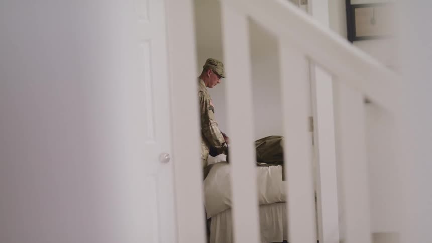 A man in a room with a military uniform putting clothing in a bag