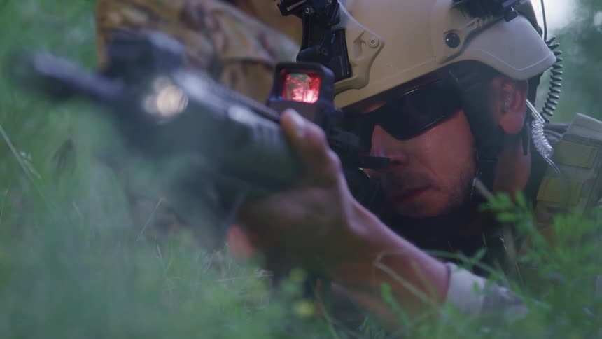 Soldier staring through a lens on a sniper rifle low down in the grass