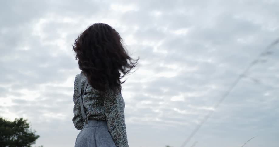 A woman runs her hand through her hair as she stands in a field on a windy day
