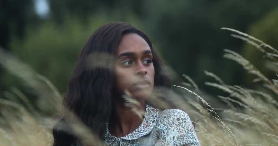 Young woman sitting in the tall yellow grass in a field near the forest at evening