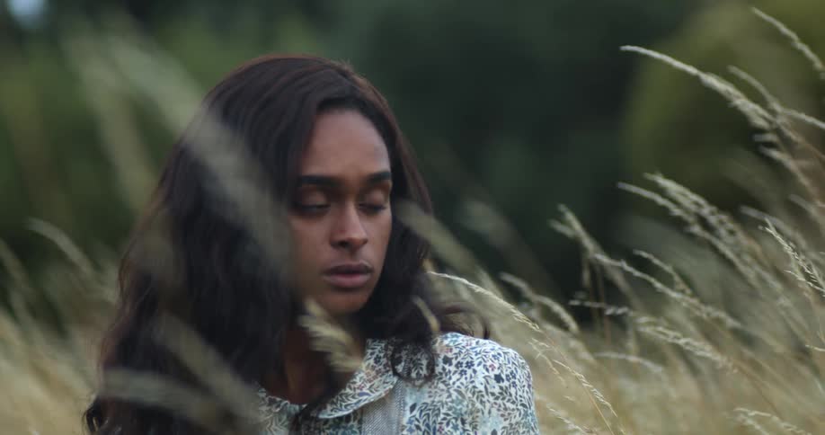 A young woman sitting in tall grass looking out at the field