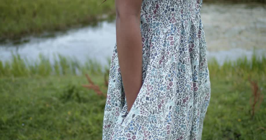 A woman stands near a large puddle in a field wearing a floral dress
