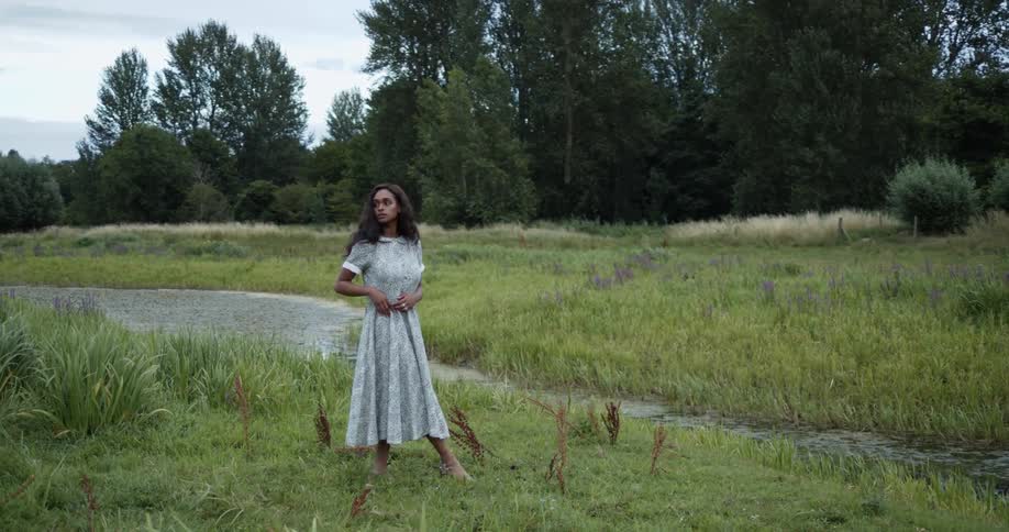 Woman standing outdoors on grass near a stream