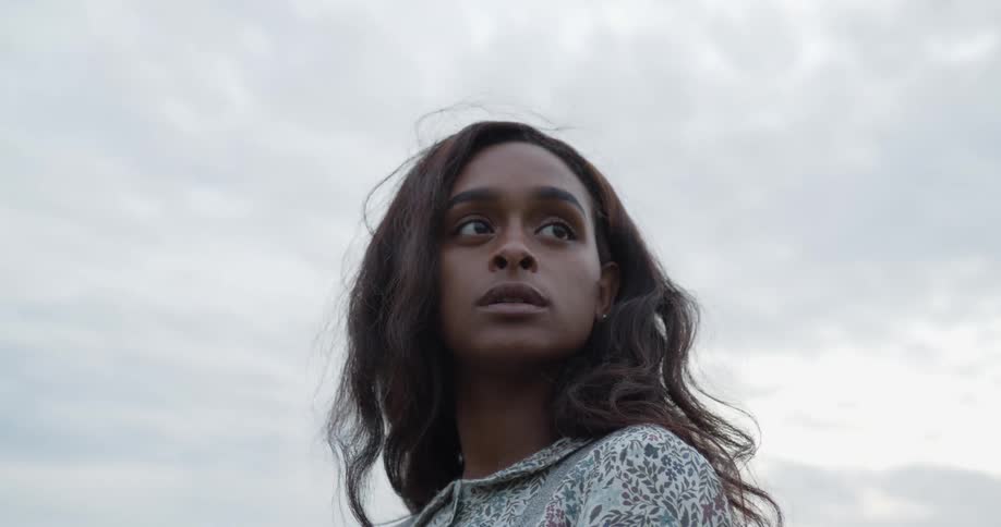 A black woman with long hair looking out across the sky