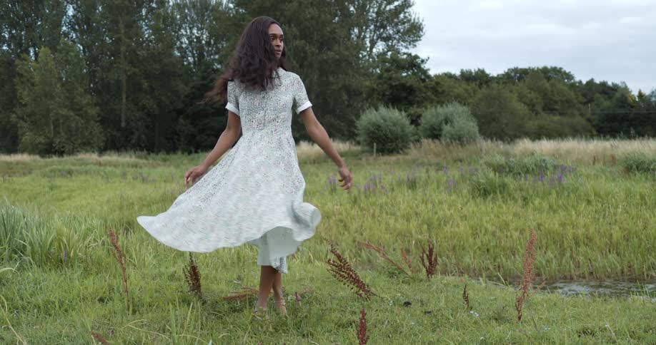 Woman spinning around in the middle of the grass field wearing a dress