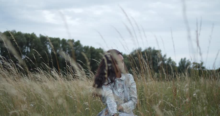 A woman sits in the tall grass on a cloudy breezy day