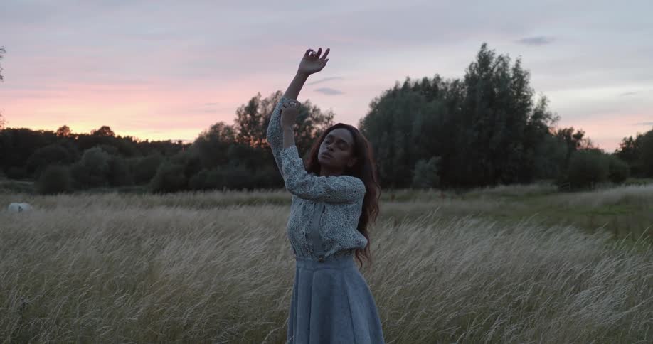 Woman posing for a photoshoot in the middle of a grass field holding her hand up