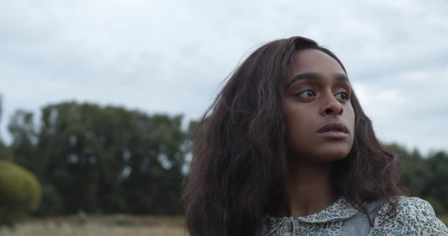 Black woman pushes her hair back with her hand as she stands outdoors near the trees
