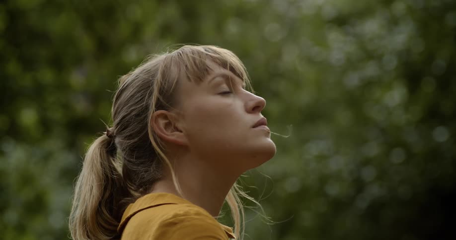 Close up of a young blonde woman face with eyes closed near the trees