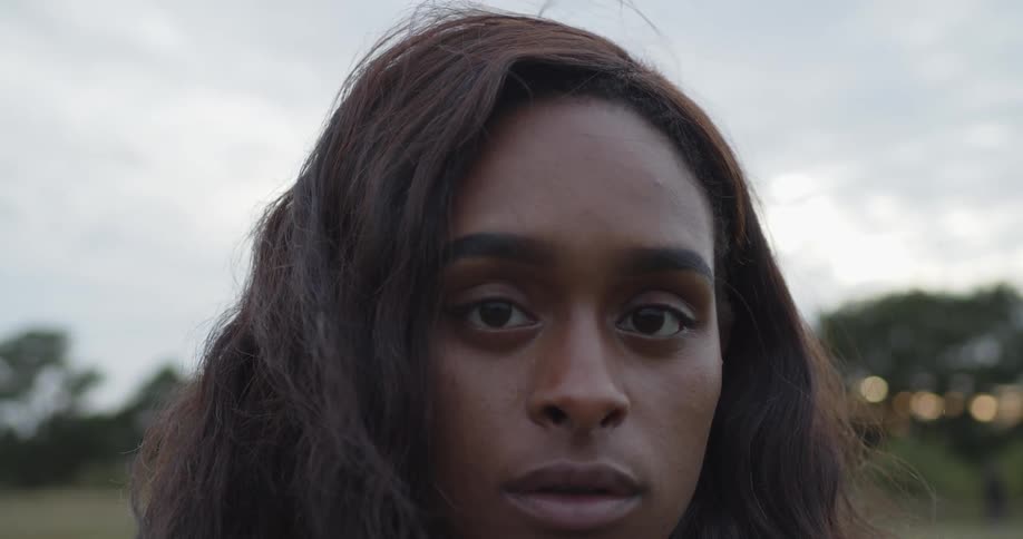 Young long haired woman standing in a green grass field looks at the camera at sunset