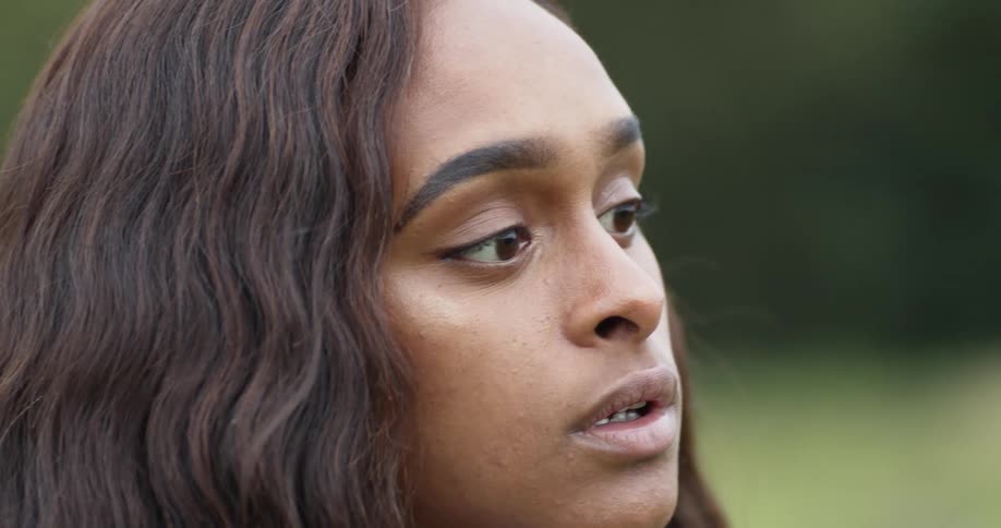 Close up of a long haired young womans face in a field at day