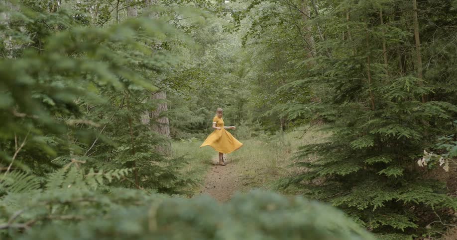 A woman with a dress in a pathway in the woods spinning