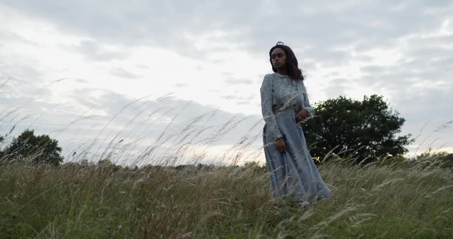 A woman standing looking off into the distance out in a grass field at daytime