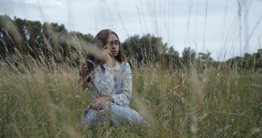 Black woman sits in a field of tall weeds