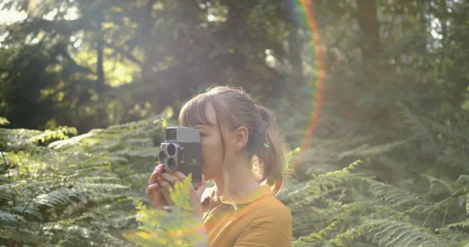 Young woman standing in the vegetation on a forest uses a vintage film camera