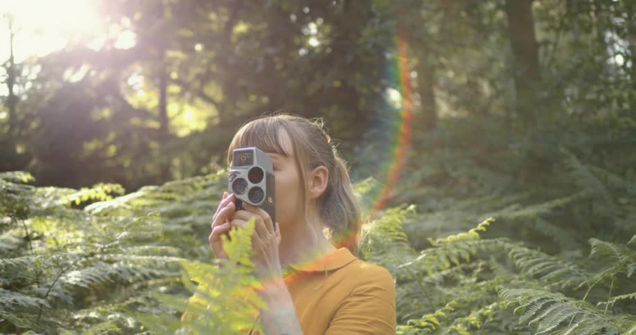 Young woman standing in the vegetation on a forest filming with a vintage camera at evening