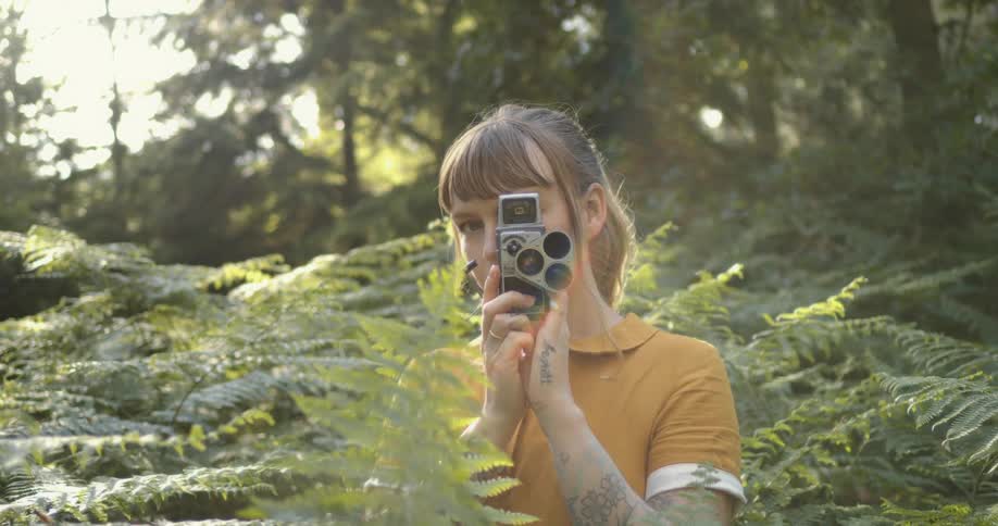 Young woman filming with a vintage camera in the forest at evening