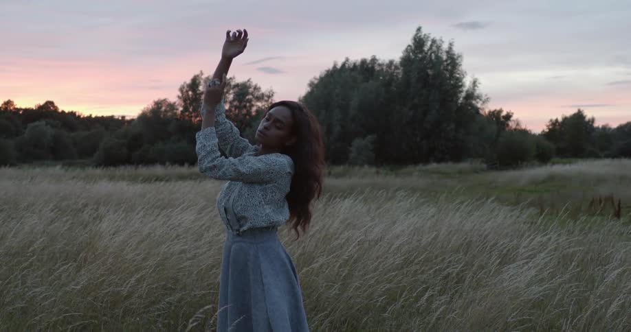Young woman standing with her arms on the air in a grass field at sunset