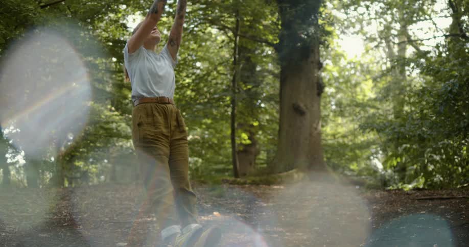 A woman in a forest pulling on something and hanging on to it at an angle