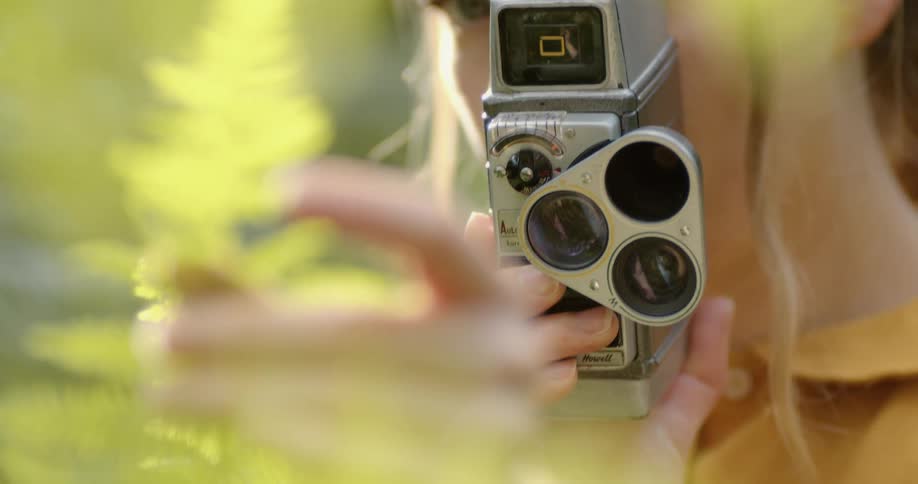 A woman is using a film camera to film a plant