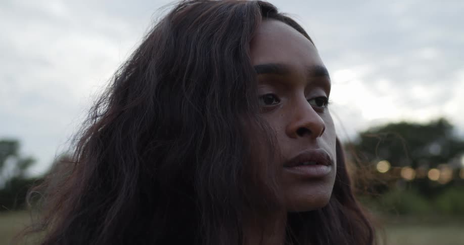 A woman brushes her hair behind her ear outdoors and turns around and looks off into the distance