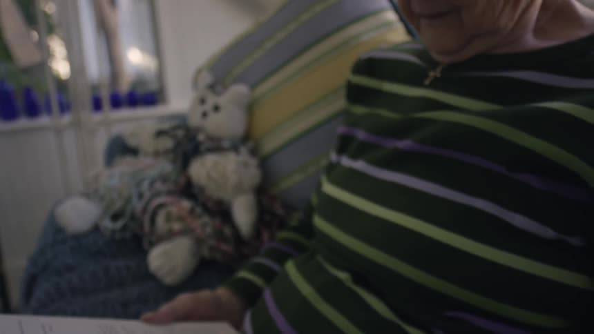 An older woman sitting on a sofa reads a book