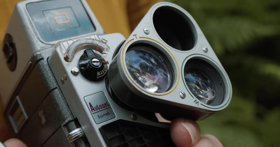 A vintage camera being help by a person outside with ferns in the background