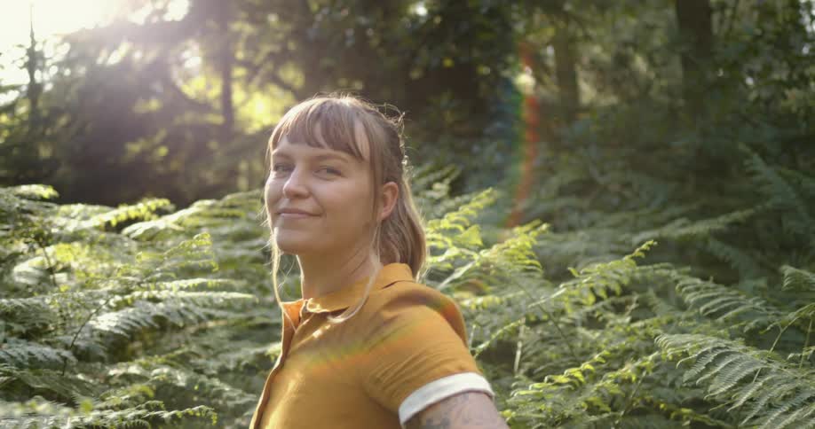 Young woman standing in the vegetation on a forest looking at the camera at evening