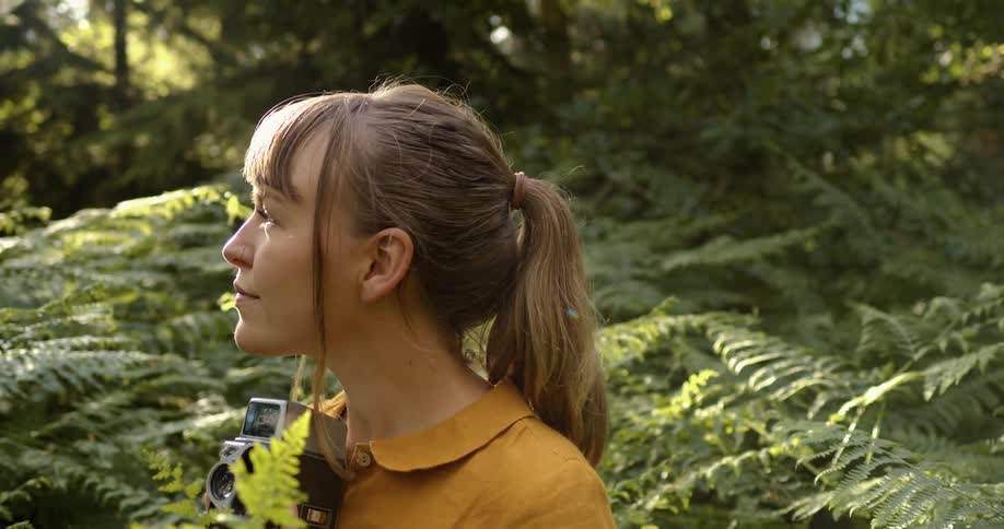A woman is standing in a forest holding a film camera