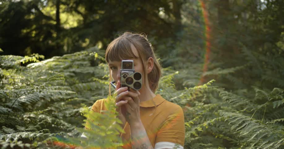 A woman poses in a jungle while holding a vintage camera