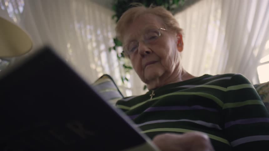 An elderly woman reads a book on a couch