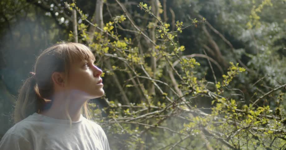 Blonde woman with pony tail and grey t shirt looks around in the forest