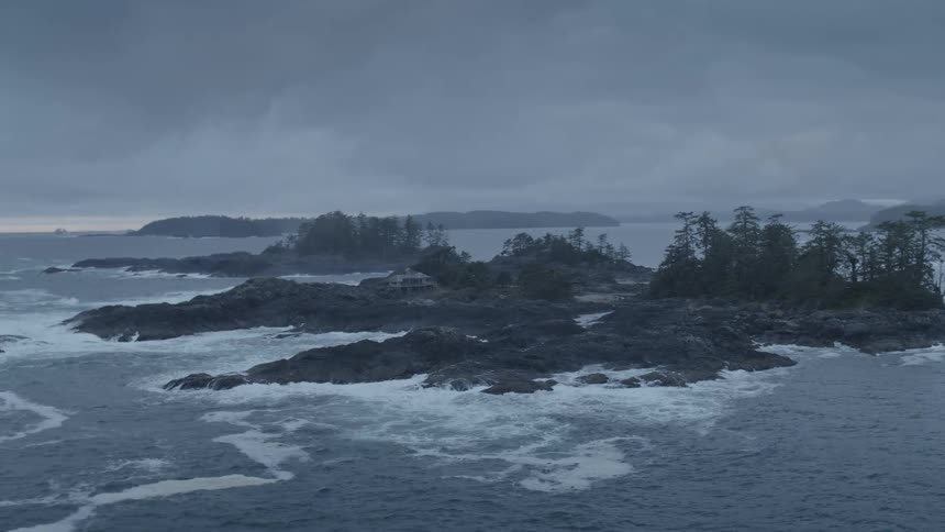 Ocean waves crash against a small rocky island with remote beach house