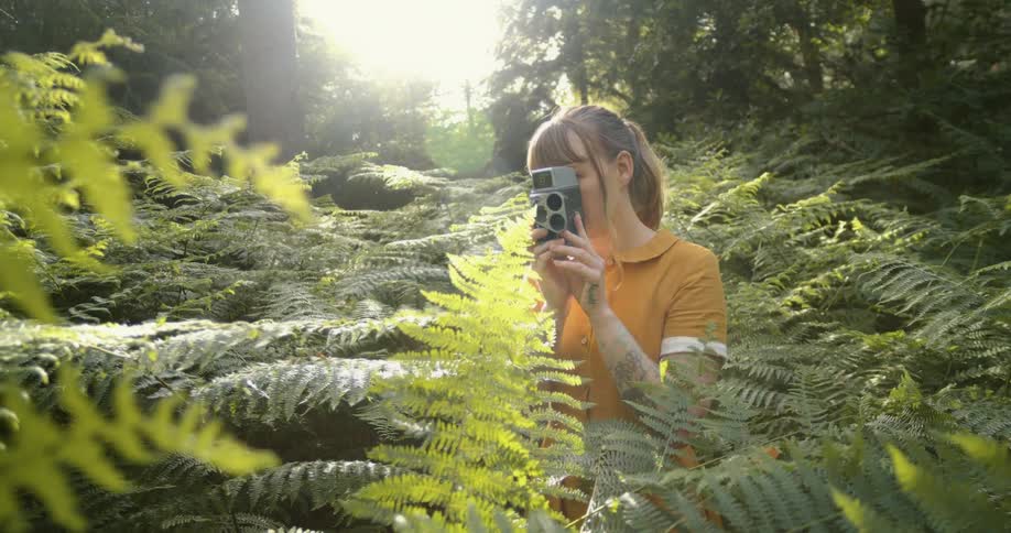 Young woman filming with a vintage camera in the forest