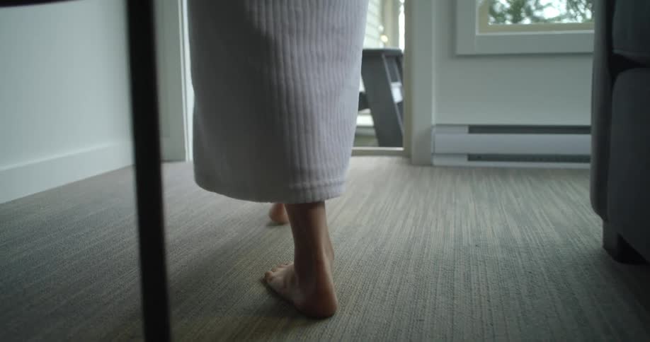 Barefoot robed woman walking from the living room to the balcony at home
