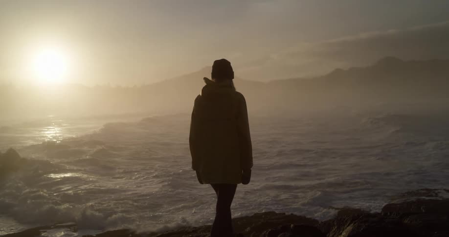 Girl walking on jagged rocks towards the ocean at sunrise