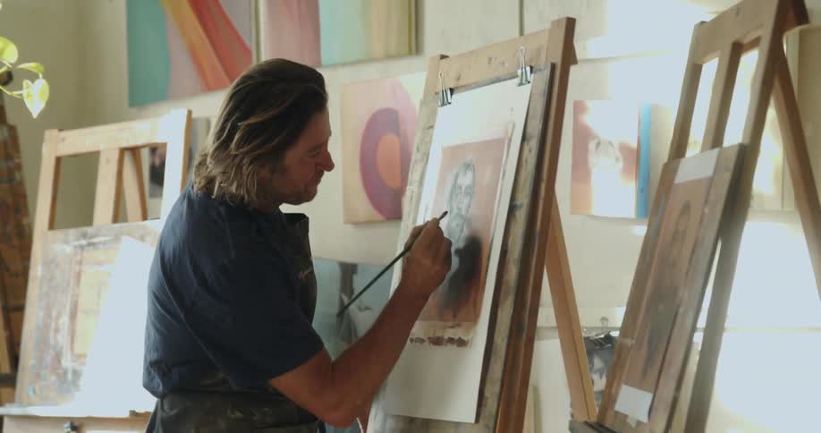 White man painting a frame wearing an apron