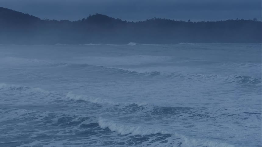 Aerial over stormy waves rolling into coast