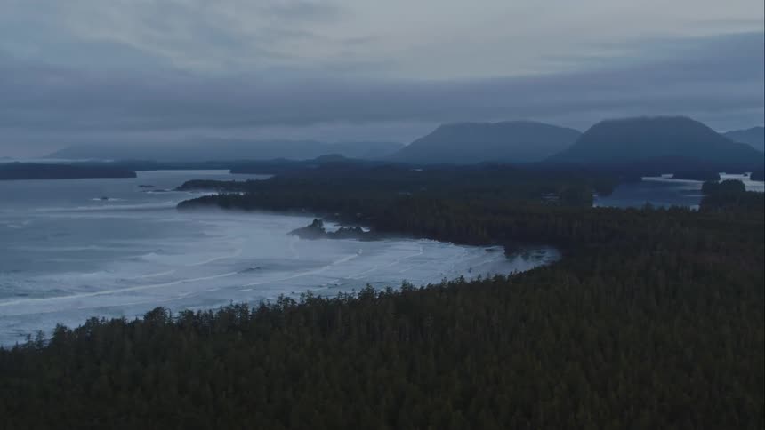 Aerial over mountain top reveals strong ocean waves moving towards the shore