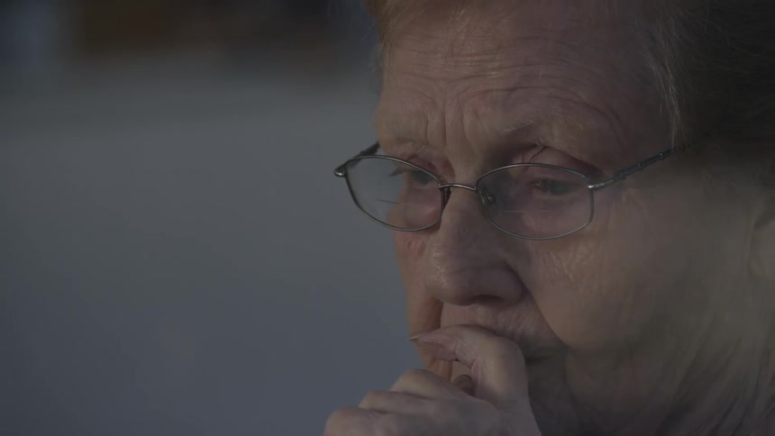 Pondering old woman rests finger against her mouth