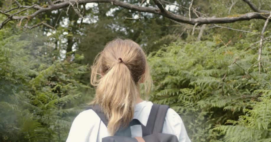 A young blonde woman walking on a trail through the forest